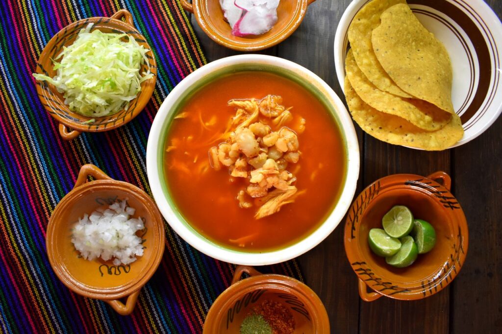 Top view of a traditional pozole soup with various fresh garnishes, perfect for authentic Mexican cuisine enthusiasts.