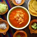 Top view of a traditional pozole soup with various fresh garnishes, perfect for authentic Mexican cuisine enthusiasts.