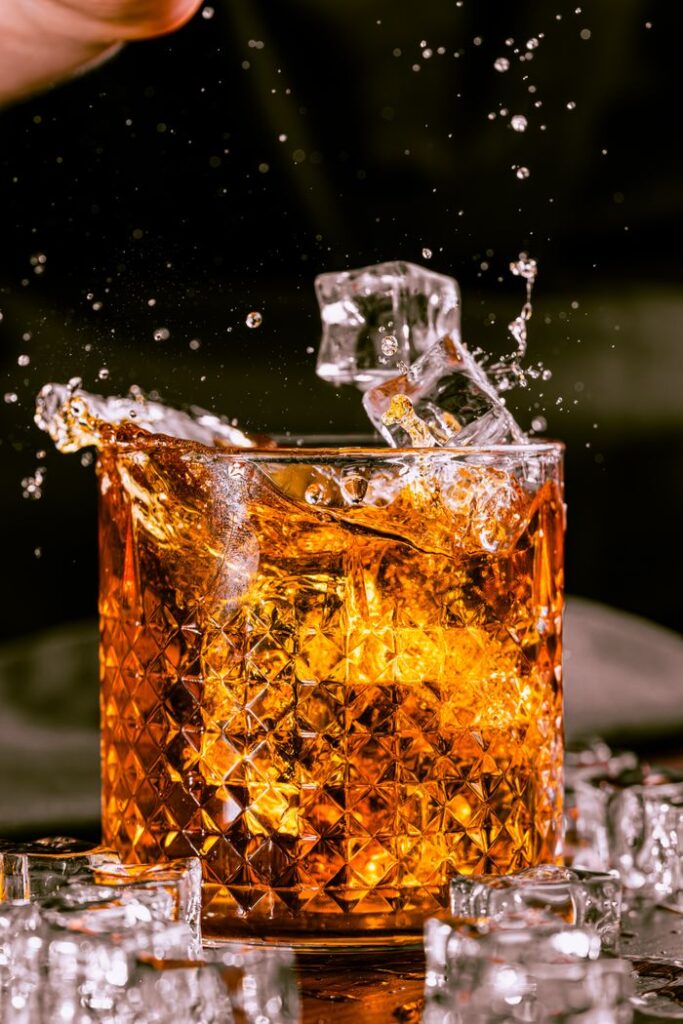 Dynamic close-up of a whiskey splash with ice cubes in a crystal glass.